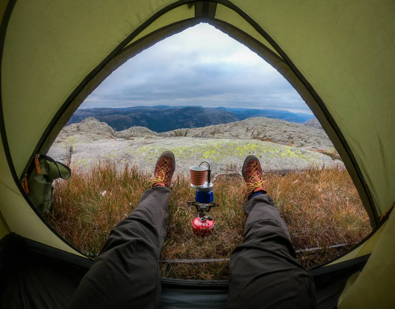 Looking out of a tent door at dawn: boots, a camping stove and a coffee pot, granite hills beyond